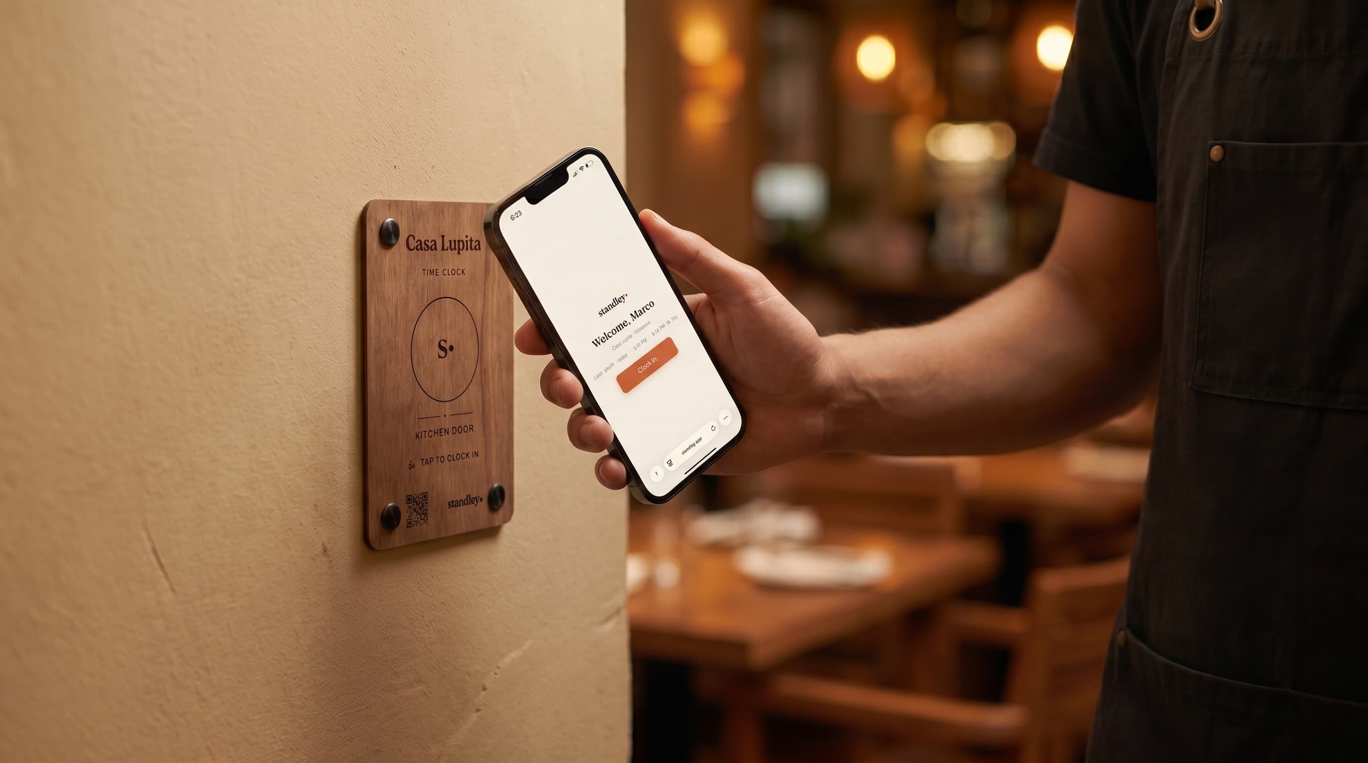 A server taps their phone on the engraved Casa Lupita clock-in station by the kitchen door; the phone shows 'Welcome, Marco' with a Clock In button